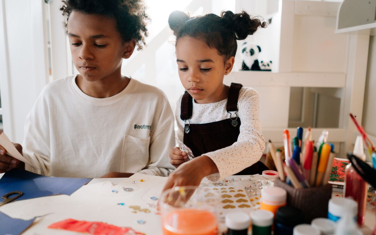 Two children engrossed in an arts and crafts workshop, surrounded by art materials indoors.
