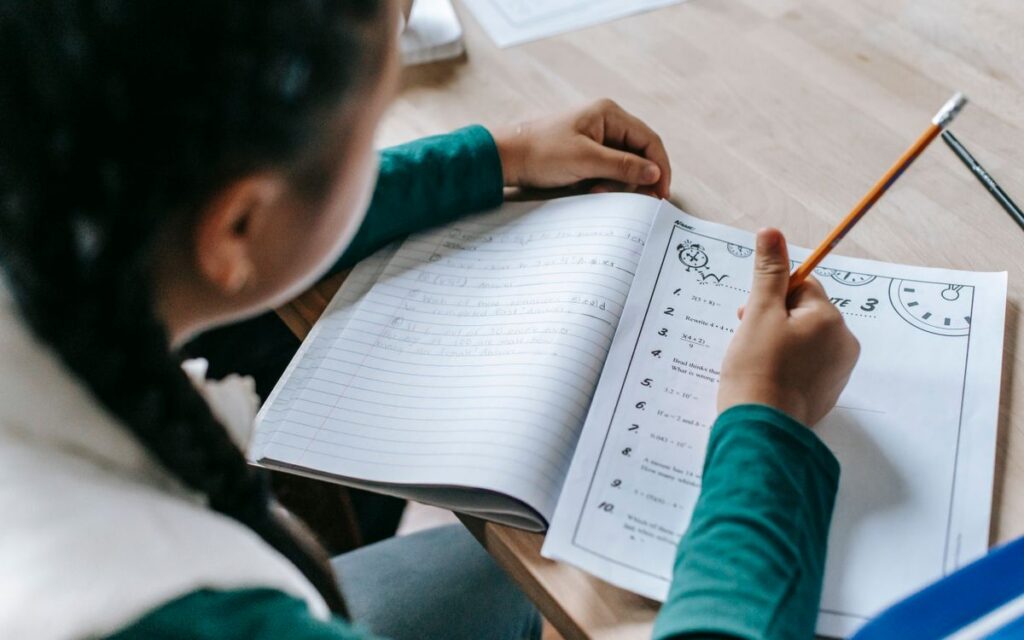 High angle crop unrecognizable schoolgirl sitting at desk with stationery and doing homework