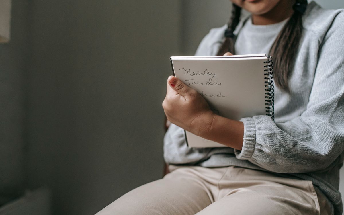 Crop unrecognizable girl in casual outfit sitting on chair and taking notes in copybook