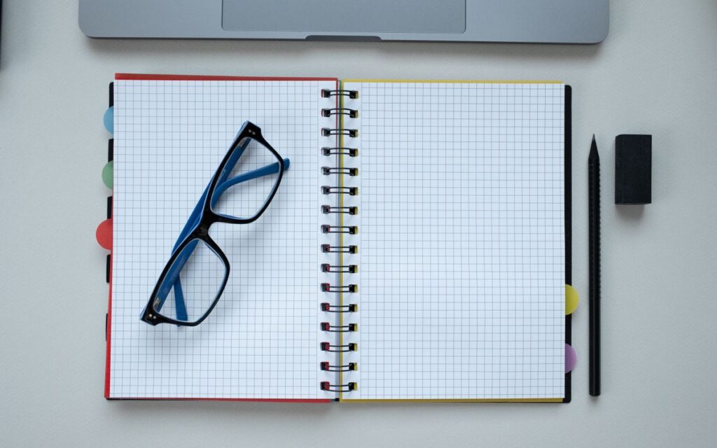 Top view of an open grid notebook, eyeglasses, and stationery arranged neatly on a desk.