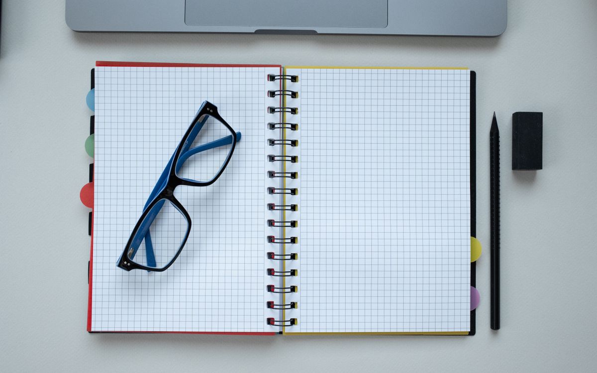 Top view of an open grid notebook, eyeglasses, and stationery arranged neatly on a desk.