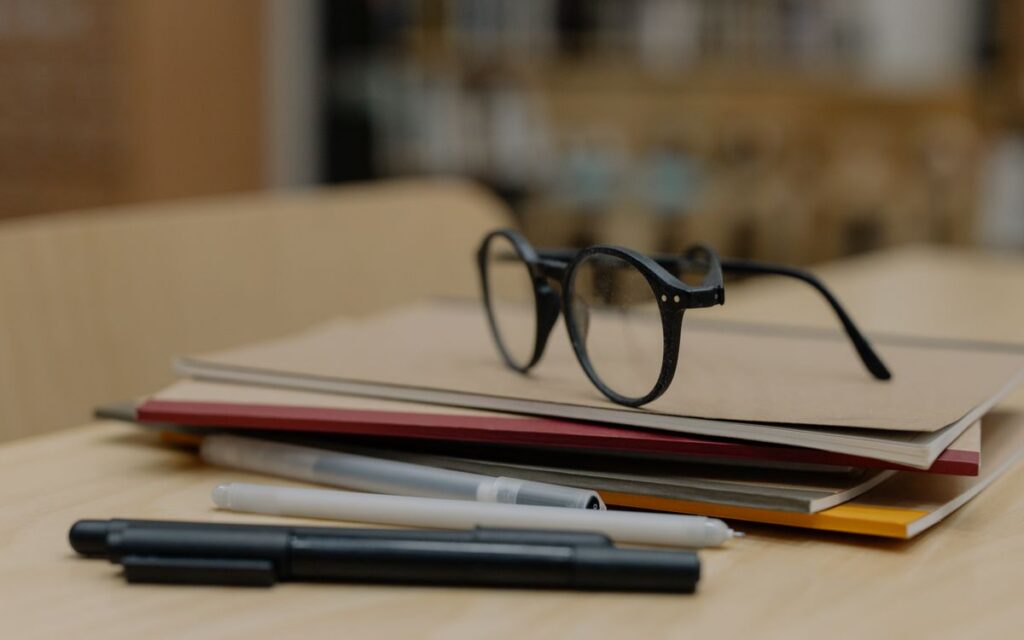 Eyeglasses resting on stacked notebooks with pens on a wooden table, perfect for education themes.