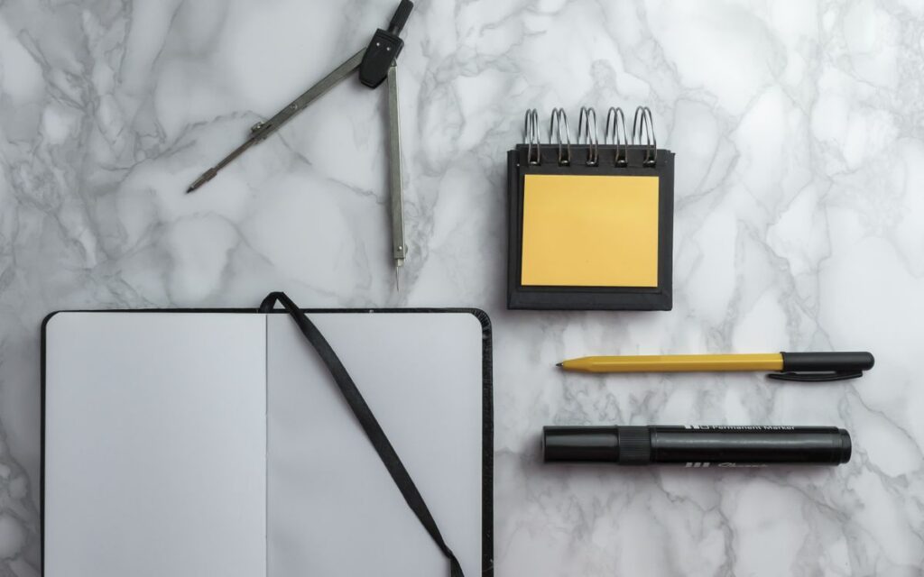 Flat lay of school supplies including compass, notebook, pen, and sticky notes on a marble surface.