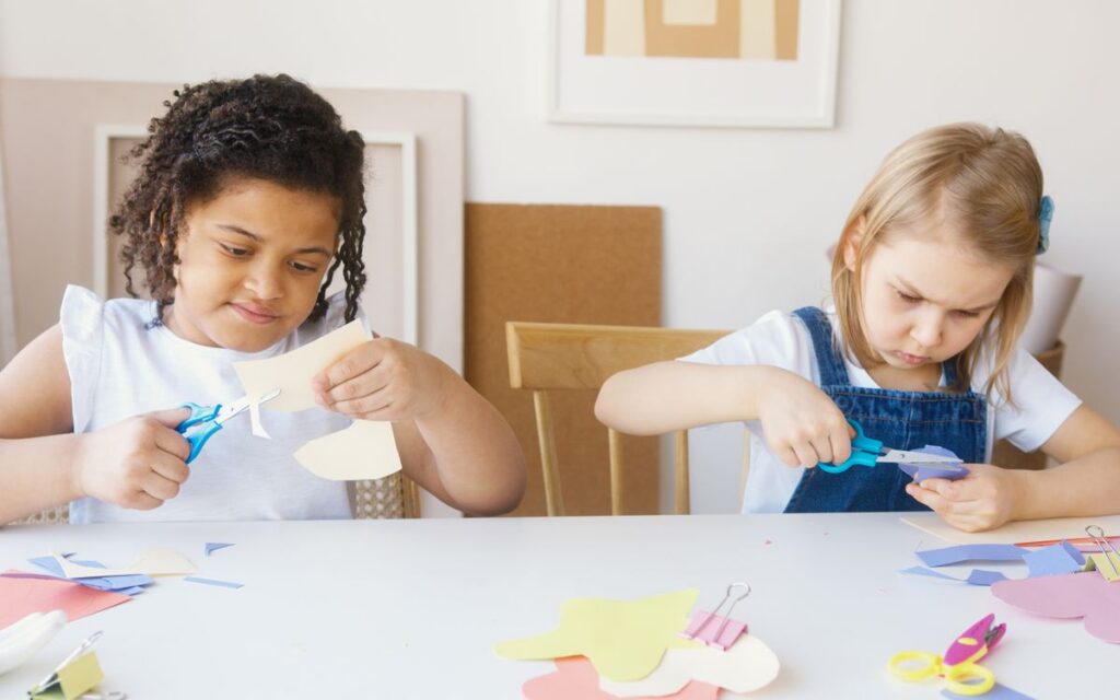 Two young girls focusing on a colorful paper crafting activity indoors.