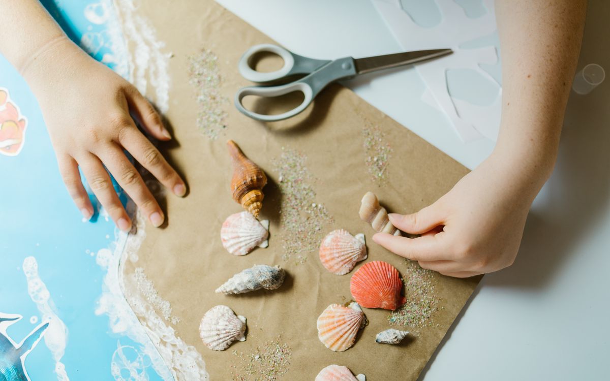 Hands arranging seashells on paper, engaging in a creative craft project.