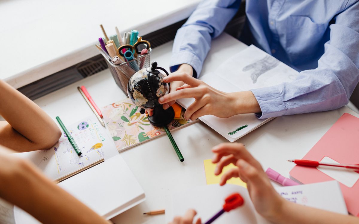 Children engaged in learning with a globe and art supplies on a desk, emphasizing education and creativity.