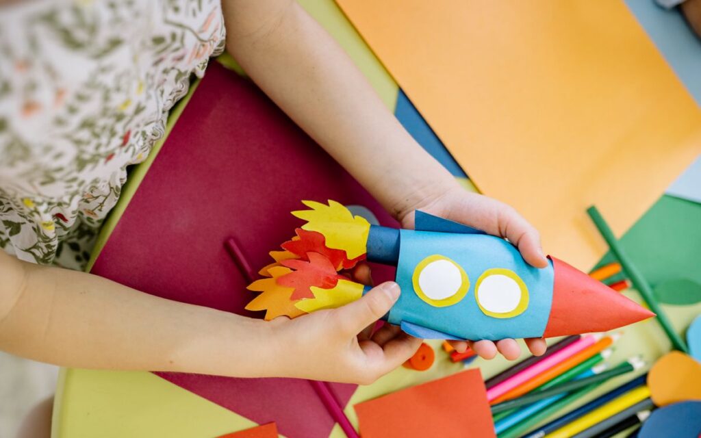 A child builds a vibrant paper rocket during an arts and crafts session, fostering creativity.