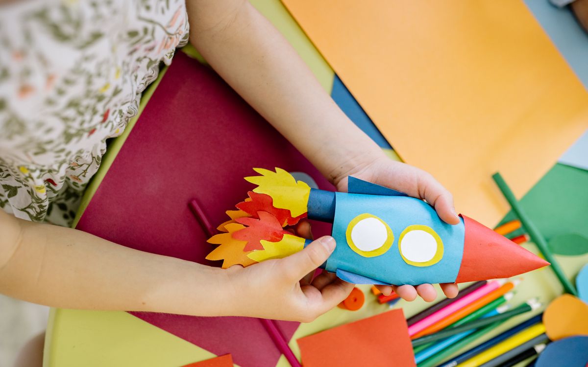 A child builds a vibrant paper rocket during an arts and crafts session, fostering creativity.