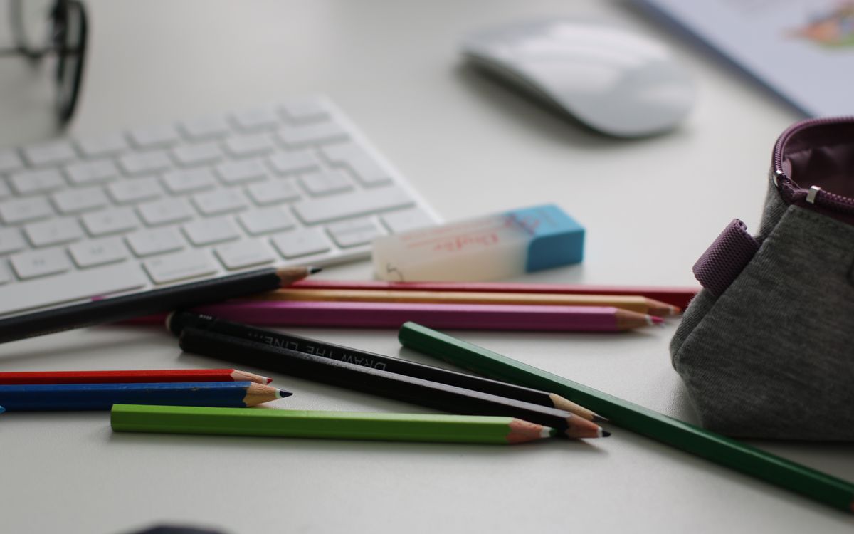 Color pencils and office supplies scattered on a white desk with keyboard and mouse.