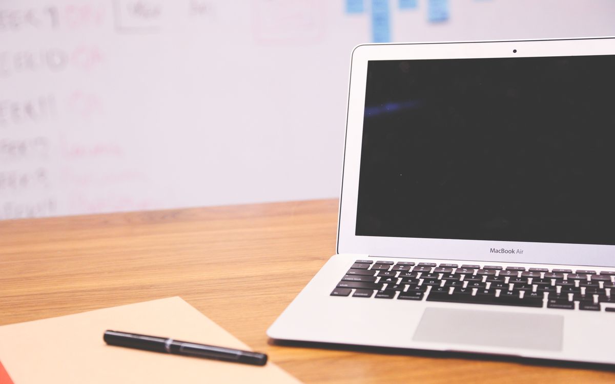 Sleek laptop on wooden desk with pen and notepad, ideal for business and tech settings.